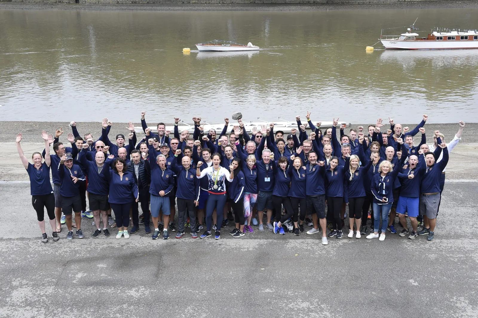 A large group of people cheering at the camera in front of a lake